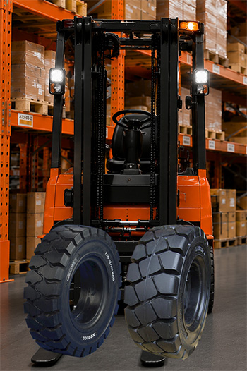 Drie volrubber banden op een rij voor een oranje heftruck in een magazijn